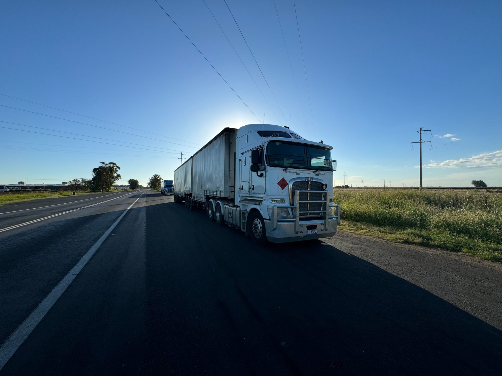 Un semi-remorque argenté circulant sur une autoroute dégagée, sous un ciel bleu limpide.
